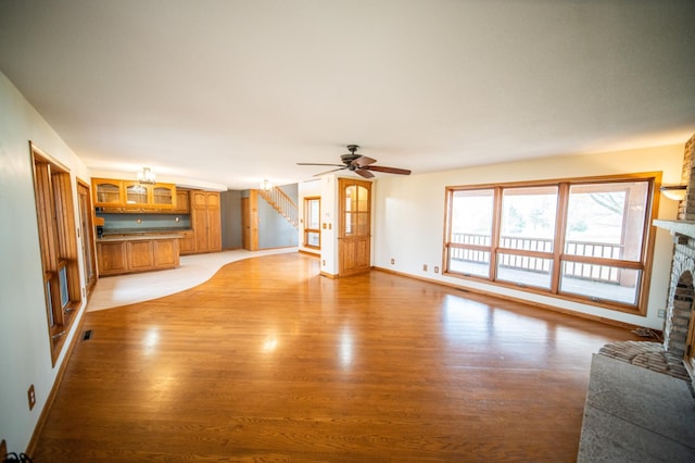 unfurnished living room with a stone fireplace, ceiling fan, and light hardwood / wood-style flooring