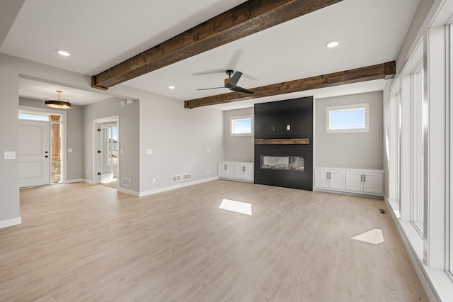 unfurnished living room with beamed ceiling, ceiling fan, light wood-type flooring, and plenty of natural light