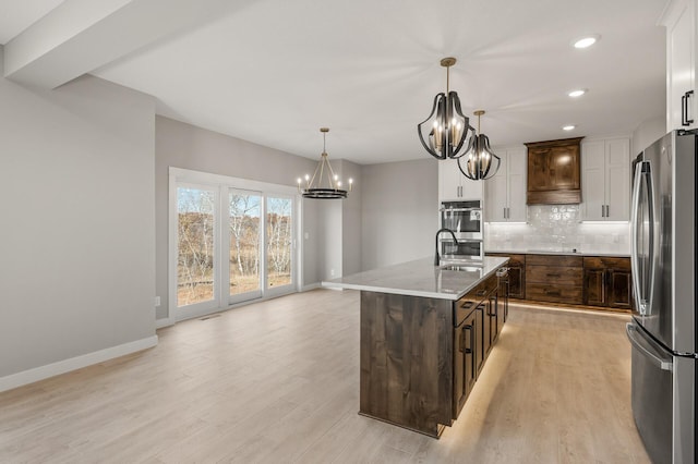 kitchen with hanging light fixtures, appliances with stainless steel finishes, a kitchen island with sink, light hardwood / wood-style floors, and dark brown cabinetry