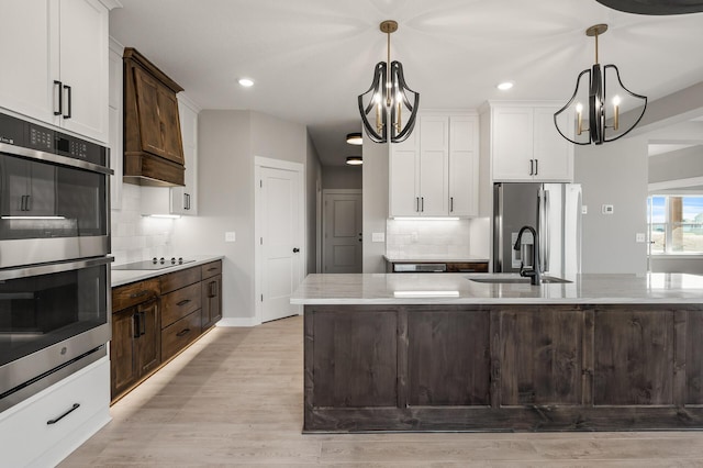 kitchen with dark brown cabinets, backsplash, light wood-type flooring, pendant lighting, and stainless steel appliances