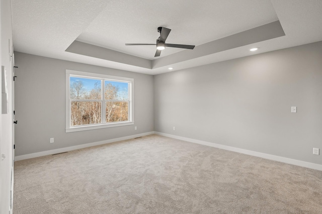 spare room featuring ceiling fan, light carpet, a textured ceiling, and a tray ceiling