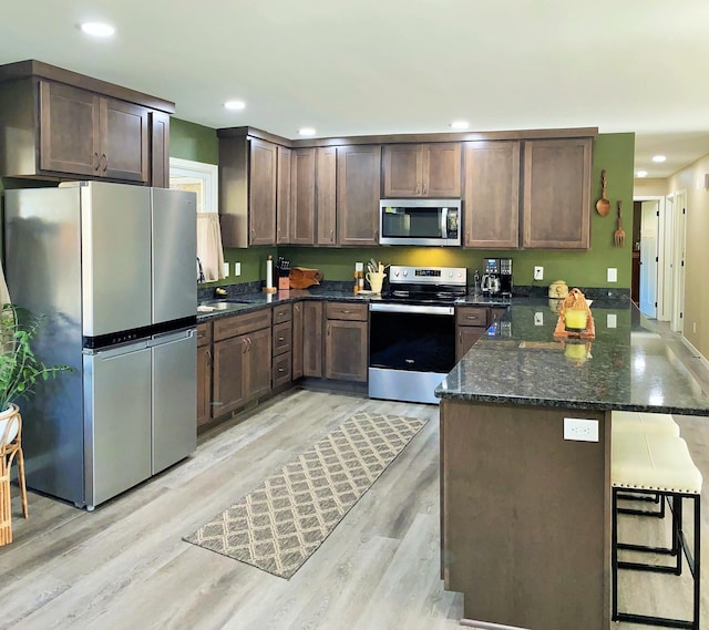 kitchen with dark stone counters, appliances with stainless steel finishes, light hardwood / wood-style floors, a kitchen bar, and kitchen peninsula