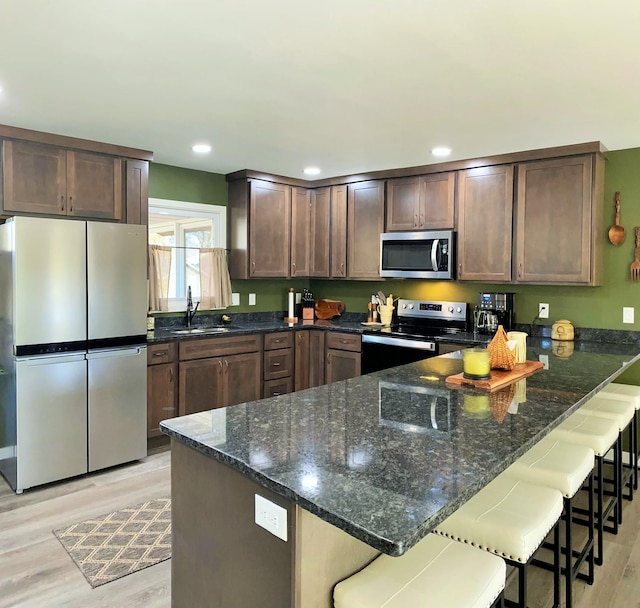 kitchen featuring a sink, stainless steel appliances, dark stone counters, a peninsula, and light wood finished floors