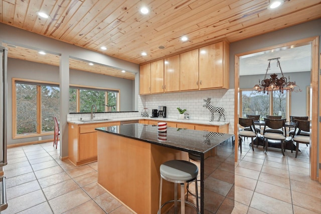 kitchen with a kitchen island, decorative backsplash, sink, an inviting chandelier, and dark stone countertops