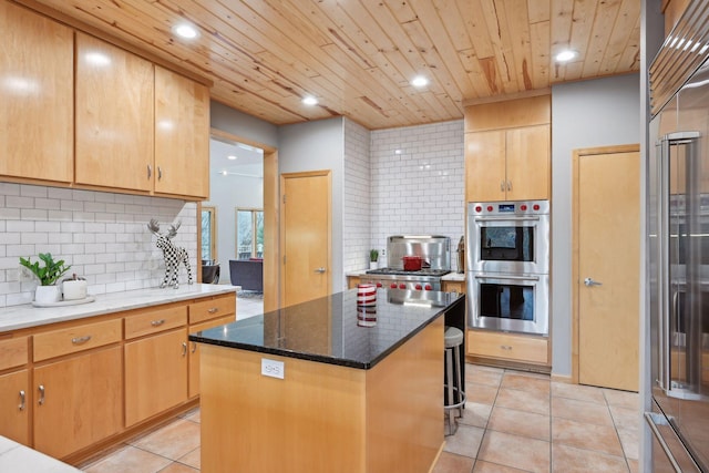 kitchen featuring stainless steel double oven, a kitchen island, backsplash, light tile patterned floors, and dark stone countertops