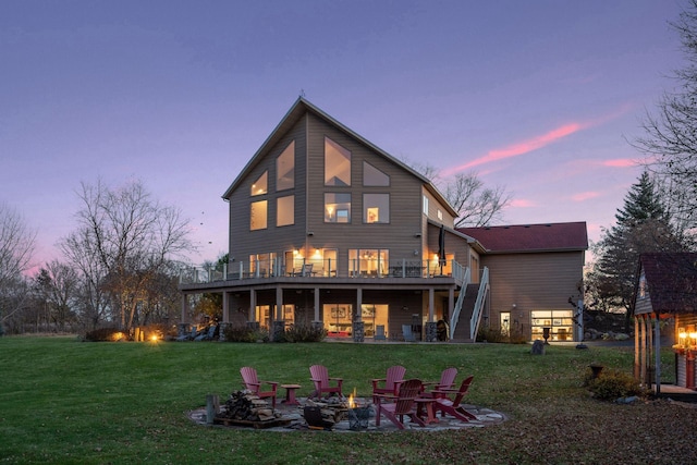 back house at dusk with a wooden deck, a yard, a fire pit, and a patio area