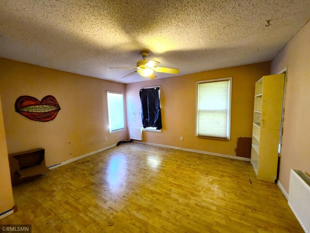 empty room with a textured ceiling, radiator, light wood-type flooring, and ceiling fan