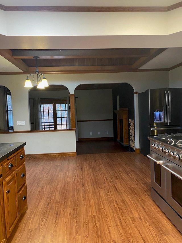 kitchen featuring appliances with stainless steel finishes, an inviting chandelier, hardwood / wood-style flooring, beamed ceiling, and crown molding