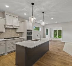 kitchen with sink, gas stovetop, an island with sink, decorative light fixtures, and white cabinets