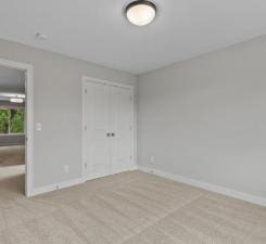 unfurnished bedroom with light colored carpet and a closet