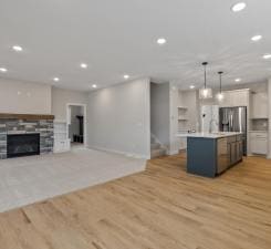 kitchen featuring a stone fireplace, a center island with sink, white cabinetry, hanging light fixtures, and stainless steel refrigerator