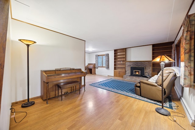 living room with built in shelves, a baseboard radiator, a brick fireplace, and light hardwood / wood-style flooring