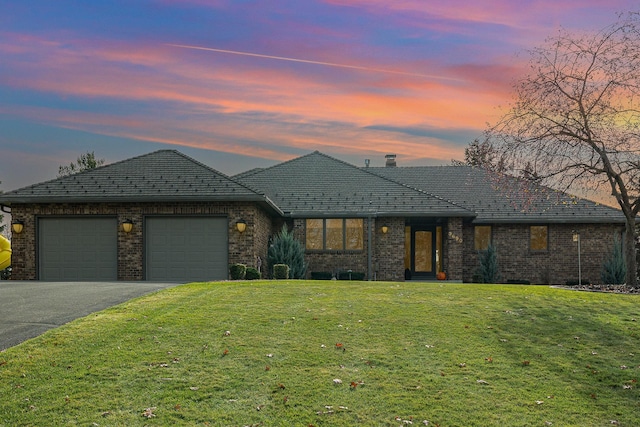 view of front of house featuring aphalt driveway, brick siding, a garage, and a front yard