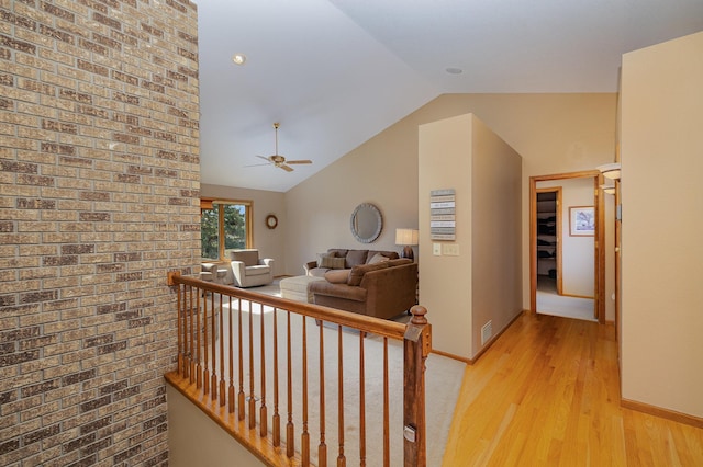 corridor featuring baseboards, an upstairs landing, lofted ceiling, and light wood-style flooring