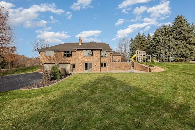 rear view of property with a lawn, aphalt driveway, a playground, an attached garage, and a chimney