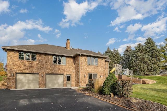 back of house with driveway, a yard, an attached garage, brick siding, and a chimney