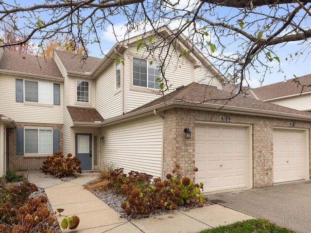 view of front of house with a garage, brick siding, a shingled roof, and aphalt driveway