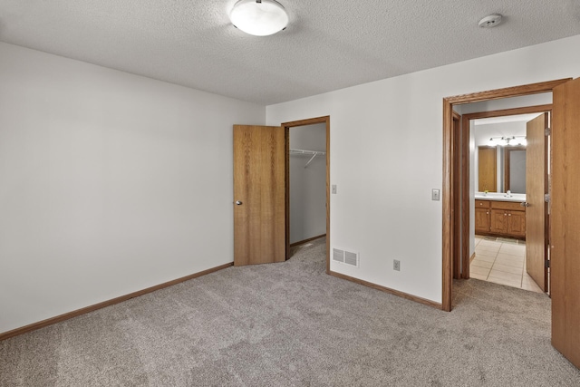 unfurnished bedroom with a closet, a spacious closet, a textured ceiling, and light colored carpet