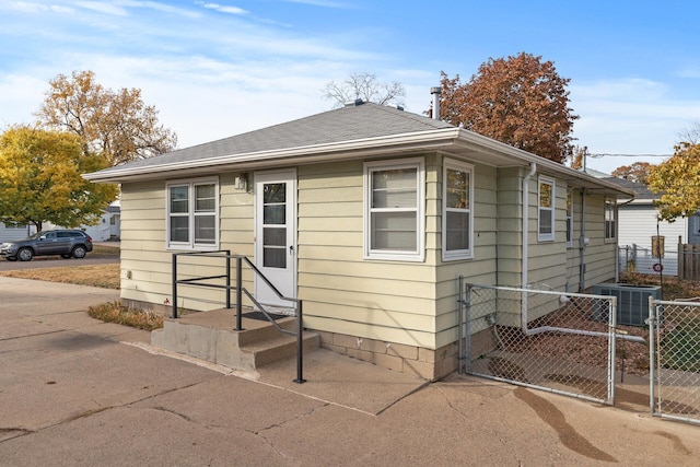 bungalow featuring cooling unit, roof with shingles, and fence