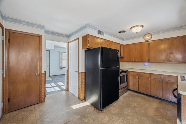 kitchen with visible vents, brown cabinets, stainless steel electric stove, and freestanding refrigerator