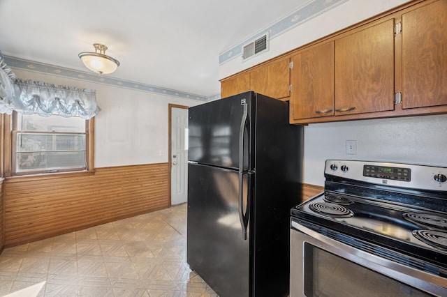 kitchen featuring visible vents, stainless steel electric stove, light floors, a wainscoted wall, and freestanding refrigerator