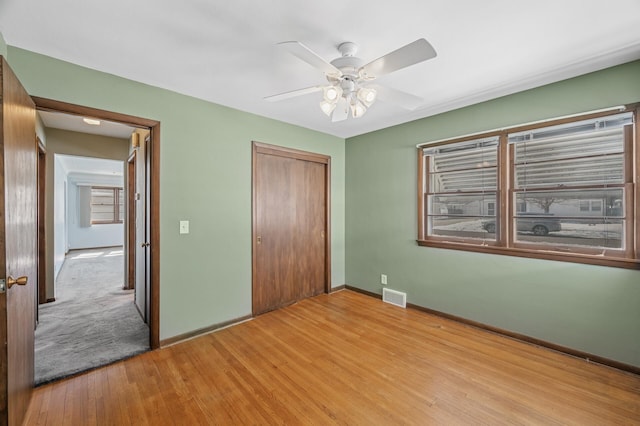 unfurnished bedroom featuring wood finished floors, visible vents, baseboards, ceiling fan, and a closet