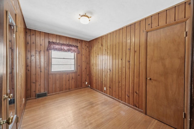 unfurnished room featuring wooden walls, light wood-style floors, visible vents, and baseboards