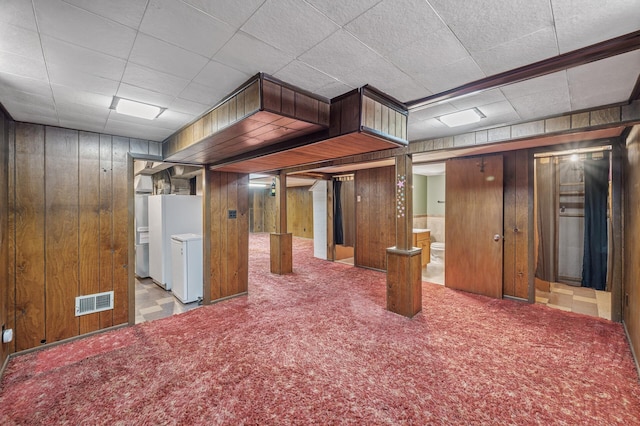 finished below grade area featuring wooden walls, carpet, visible vents, and freestanding refrigerator