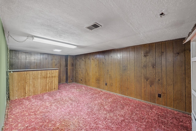 finished below grade area with visible vents, a textured ceiling, wood walls, and carpet flooring