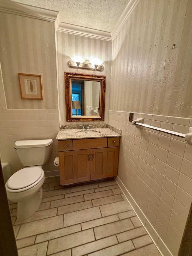 bathroom featuring a textured ceiling, toilet, tile walls, vanity, and ornamental molding