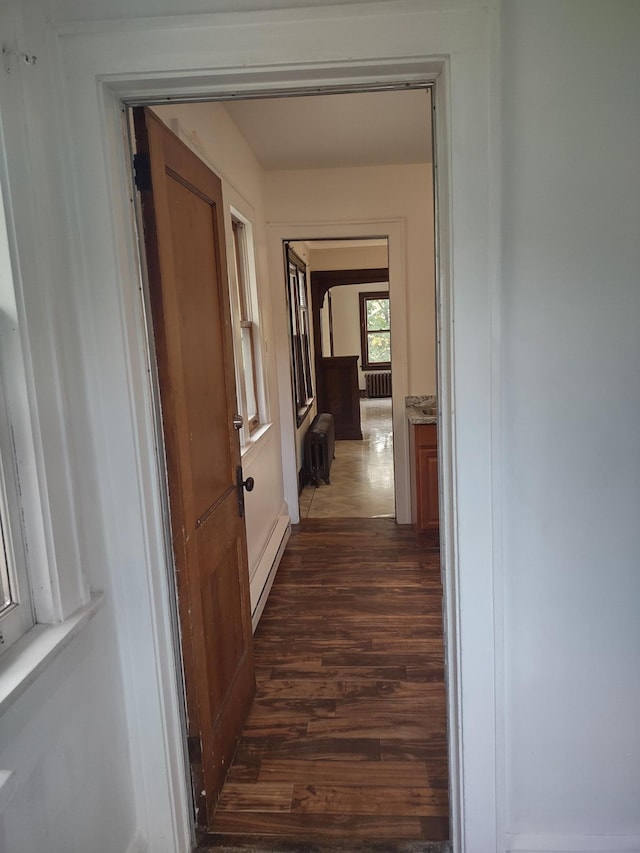 corridor with dark wood-type flooring and a baseboard heating unit