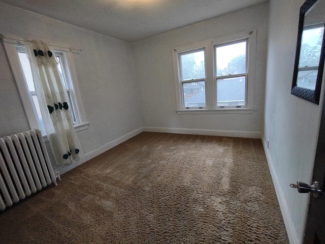 spare room with carpet, a textured ceiling, and radiator