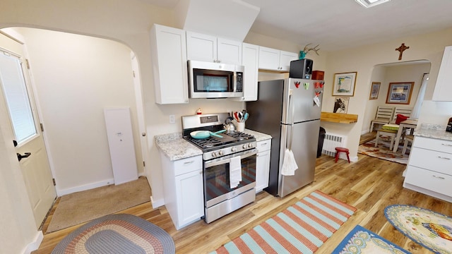 kitchen with radiator, light hardwood / wood-style flooring, light stone countertops, white cabinetry, and appliances with stainless steel finishes