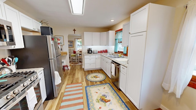 kitchen with appliances with stainless steel finishes, white cabinets, and light hardwood / wood-style flooring