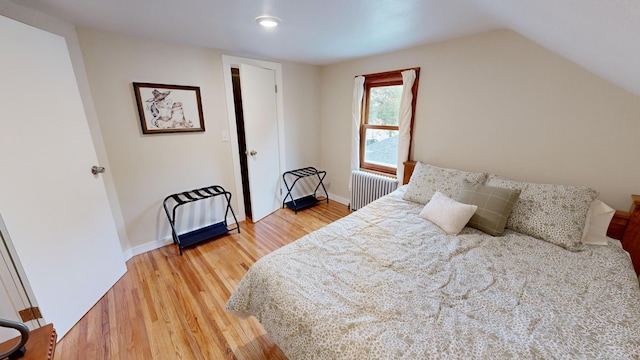 bedroom with hardwood / wood-style flooring, radiator, and vaulted ceiling