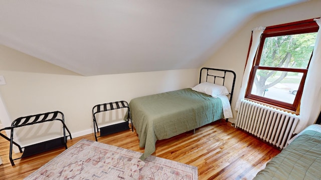 bedroom with lofted ceiling, radiator heating unit, and light wood-type flooring