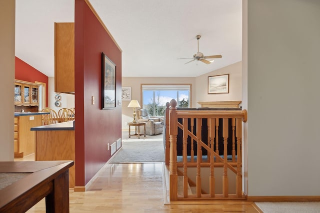 corridor with light wood-type flooring, lofted ceiling, visible vents, and baseboards