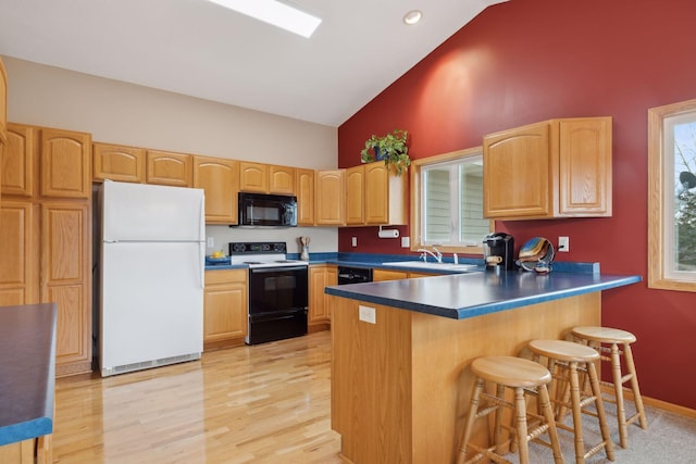 kitchen featuring a sink, a peninsula, black appliances, and light wood finished floors