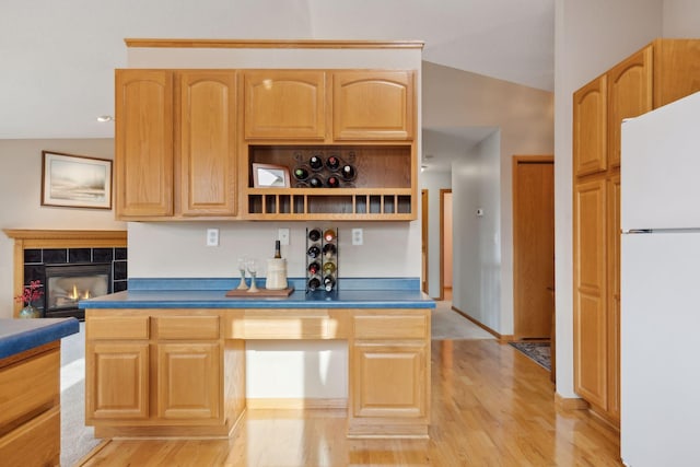 kitchen with freestanding refrigerator, vaulted ceiling, a tiled fireplace, and light wood finished floors