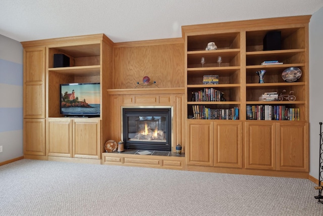 unfurnished living room with carpet floors, a glass covered fireplace, and baseboards