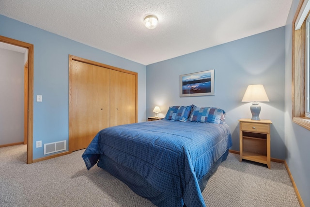 carpeted bedroom with a closet, visible vents, a textured ceiling, and baseboards