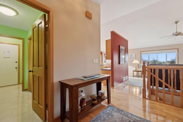 hallway featuring light wood-style floors, visible vents, and a textured ceiling