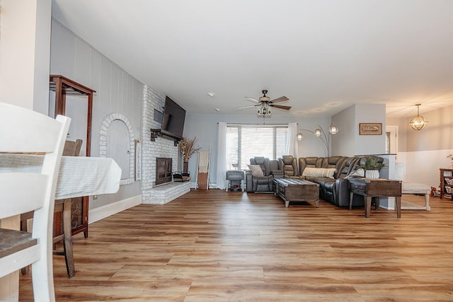 living room with a brick fireplace, ceiling fan, and light hardwood / wood-style flooring