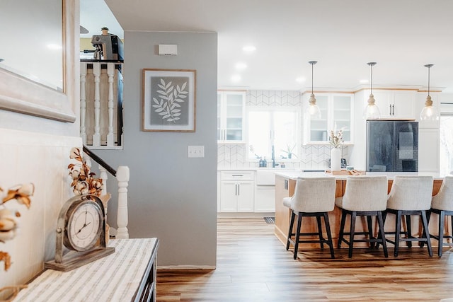 kitchen with decorative backsplash, black fridge, white cabinets, and decorative light fixtures