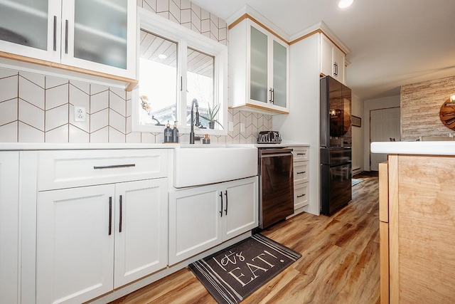 kitchen featuring light wood-type flooring, white cabinets, sink, and backsplash