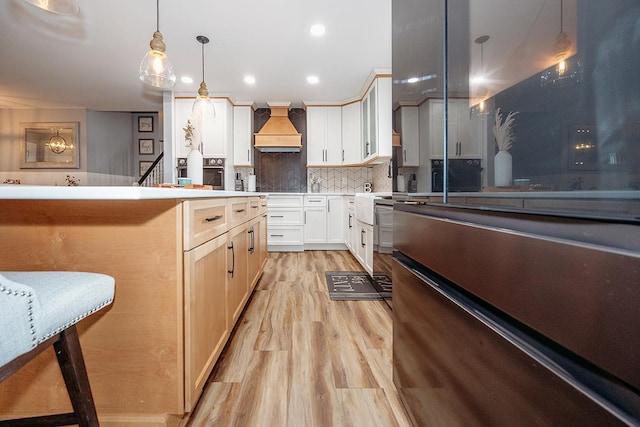 kitchen featuring white cabinetry, decorative light fixtures, light wood-type flooring, a kitchen breakfast bar, and custom range hood