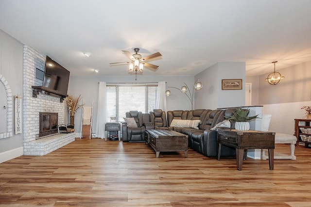 living room with ceiling fan with notable chandelier, a fireplace, and light hardwood / wood-style floors