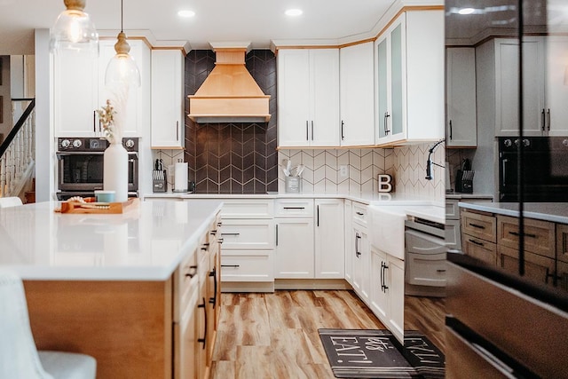 kitchen featuring white cabinetry, premium range hood, hanging light fixtures, and oven