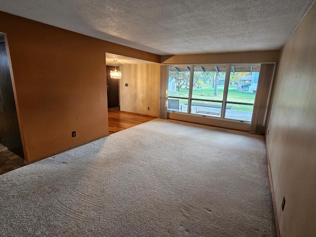 spare room featuring an inviting chandelier, a textured ceiling, and carpet floors