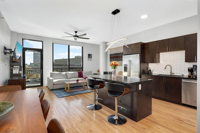 kitchen with appliances with stainless steel finishes, a kitchen island, a breakfast bar area, decorative light fixtures, and light hardwood / wood-style flooring